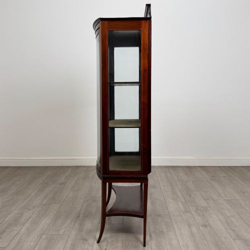 fig 3. An Edwardian mahogany display cabinet with a bow-front glazed door, fabric-lined interior shelves, marquetry inlay, and slender tapered legs with a lower shelf.