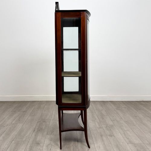fig 7. An Edwardian mahogany display cabinet with a bow-front glazed door, fabric-lined interior shelves, marquetry inlay, and slender tapered legs with a lower shelf.