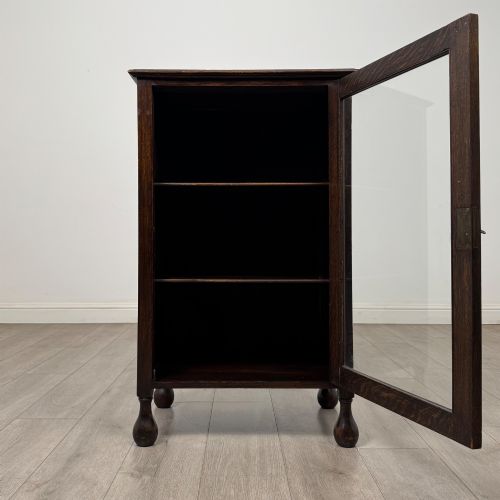 fig 1. An Edwardian dark brown oak display cabinet featuring a single glazed door and turned feet.