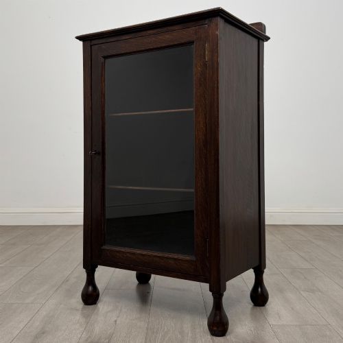 fig 2. An Edwardian dark brown oak display cabinet featuring a single glazed door and turned feet.