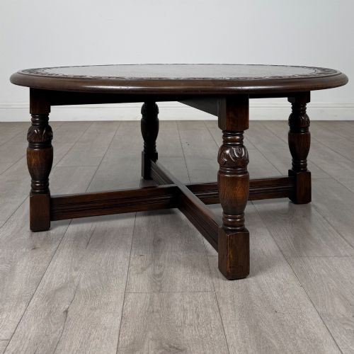 fig 1. A low circular dark oak coffee table featuring carved turned legs, an X-shaped cross stretcher, and a carved geometric border along the top rim.