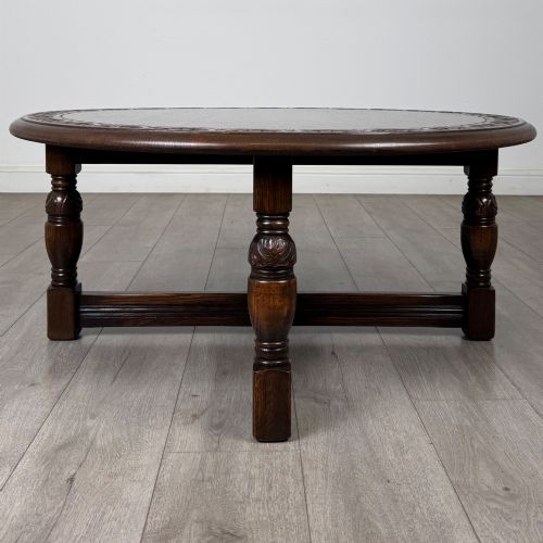 fig 2. A low circular dark oak coffee table featuring carved turned legs, an X-shaped cross stretcher, and a carved geometric border along the top rim.