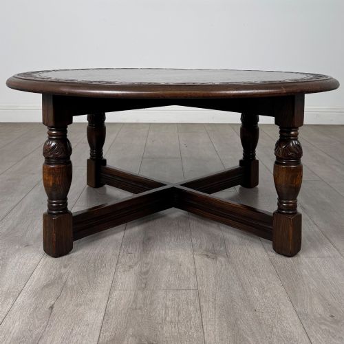 fig 3. A low circular dark oak coffee table featuring carved turned legs, an X-shaped cross stretcher, and a carved geometric border along the top rim.