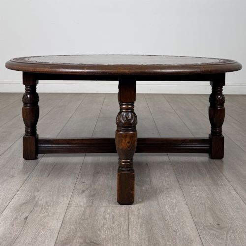 fig 4. A low circular dark oak coffee table featuring carved turned legs, an X-shaped cross stretcher, and a carved geometric border along the top rim.