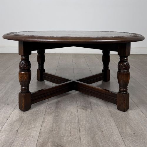 fig 5. A low circular dark oak coffee table featuring carved turned legs, an X-shaped cross stretcher, and a carved geometric border along the top rim.