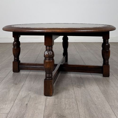 fig 6. A low circular dark oak coffee table featuring carved turned legs, an X-shaped cross stretcher, and a carved geometric border along the top rim.