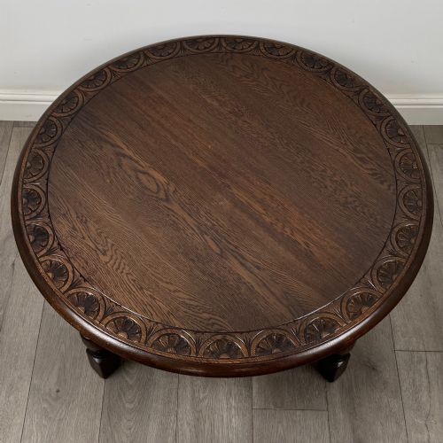 fig 7. A low circular dark oak coffee table featuring carved turned legs, an X-shaped cross stretcher, and a carved geometric border along the top rim.