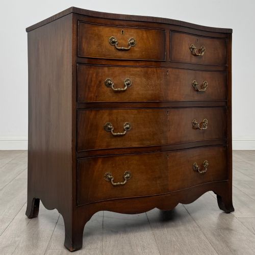 fig 7. A mahogany serpentine chest of drawers featuring four graduating drawer tiers with brass handles and a curved front profile.