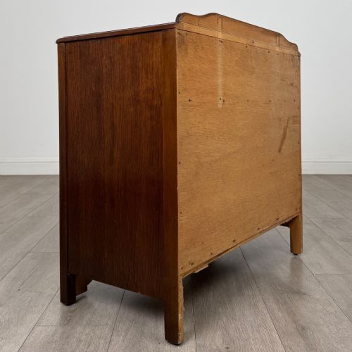 fig 3. A dark brown oak chest of drawers featuring three wide drawers with ornamental metal drop handles and a carved geometric frieze along the top edge.