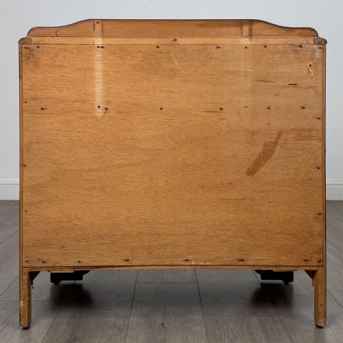 fig 4. A dark brown oak chest of drawers featuring three wide drawers with ornamental metal drop handles and a carved geometric frieze along the top edge.