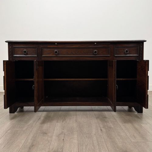 fig 1. A dark oak sideboard featuring carved linenfold central doors flanked by eight drawers with metal drop ring handles.