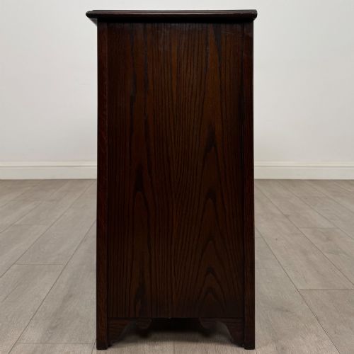 fig 3. A dark oak sideboard featuring carved linenfold central doors flanked by eight drawers with metal drop ring handles.