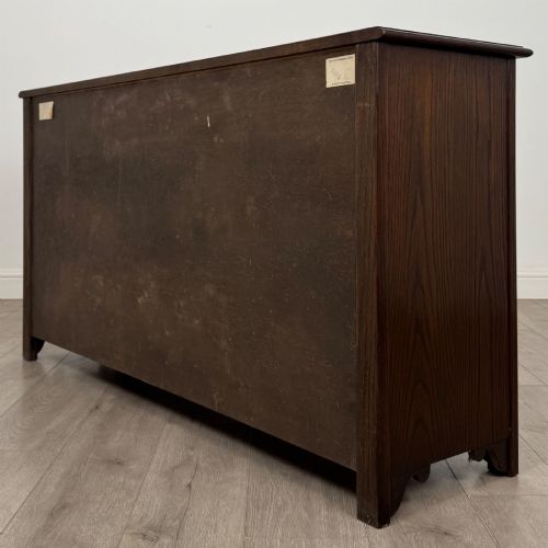 fig 6. A dark oak sideboard featuring carved linenfold central doors flanked by eight drawers with metal drop ring handles.