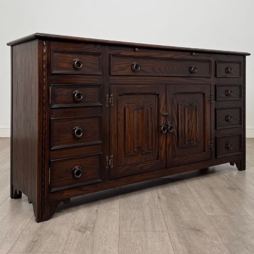 fig 8. A dark oak sideboard featuring carved linenfold central doors flanked by eight drawers with metal drop ring handles.