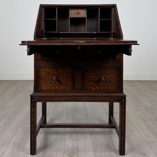 fig 1. A small Edwardian dark oak writing bureau on a tall stand with two drawers featuring carved central panels and turned knobs.