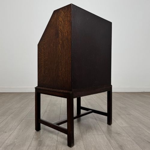 fig 4. A small Edwardian dark oak writing bureau on a tall stand with two drawers featuring carved central panels and turned knobs.
