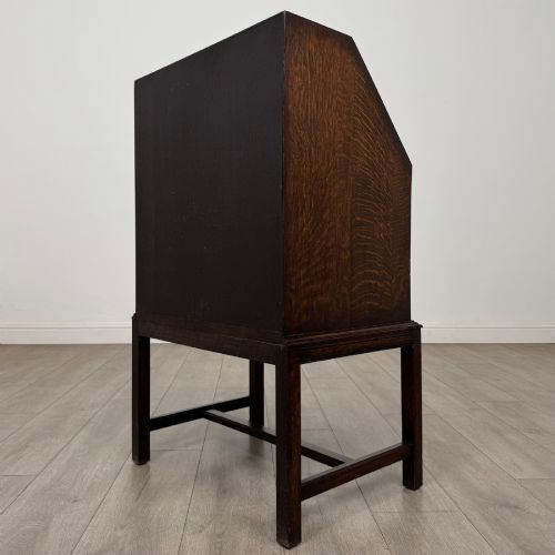 fig 6. A small Edwardian dark oak writing bureau on a tall stand with two drawers featuring carved central panels and turned knobs.