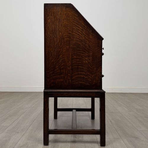 fig 7. A small Edwardian dark oak writing bureau on a tall stand with two drawers featuring carved central panels and turned knobs.