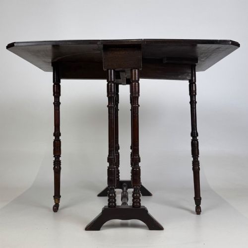 fig 4. A twentieth-century dark mahogany drop-leaf table featuring turned legs, a central stretcher rail, and folding side flaps.