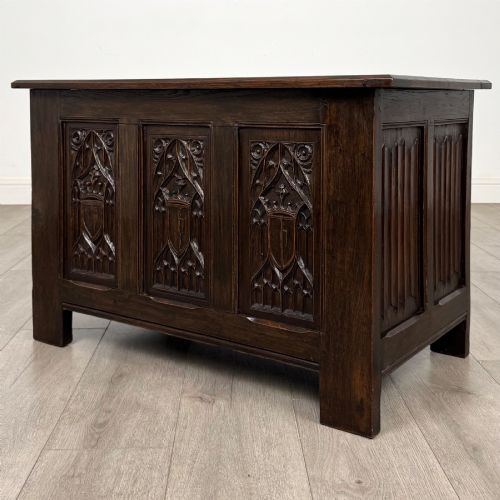 fig 1. A dark oak blanket box featuring three front panels decorated with detailed Gothic arch and shield carvings.