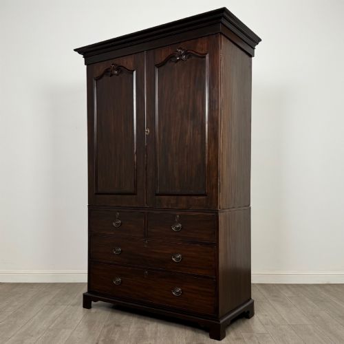 fig 2. A tall 19th-century dark mahogany linen press featuring carved panelled doors on top and a chest of four drawers at the base.