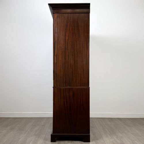 fig 3. A tall 19th-century dark mahogany linen press featuring carved panelled doors on top and a chest of four drawers at the base.