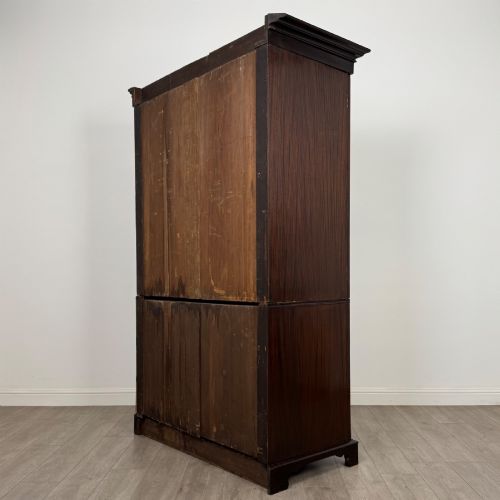 fig 6. A tall 19th-century dark mahogany linen press featuring carved panelled doors on top and a chest of four drawers at the base.