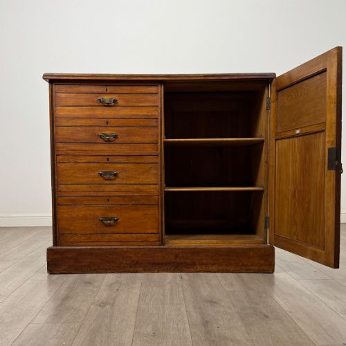 fig 1. A nineteenth-century warm brown ash wood cupboard featuring four drawers on the left and a panelled cupboard door on the right resting on a plinth base.