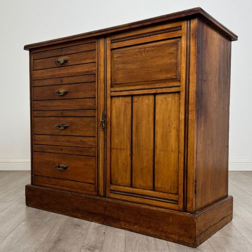 fig 2. A nineteenth-century warm brown ash wood cupboard featuring four drawers on the left and a panelled cupboard door on the right resting on a plinth base.