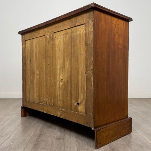 fig 6. A nineteenth-century warm brown ash wood cupboard featuring four drawers on the left and a panelled cupboard door on the right resting on a plinth base.