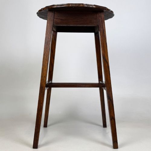 fig 2. A tall, dark oak Edwardian side table featuring a scalloped piecrust rim top, four splayed square legs, and a lower slatted shelf.