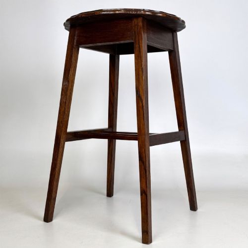fig 3. A tall, dark oak Edwardian side table featuring a scalloped piecrust rim top, four splayed square legs, and a lower slatted shelf.