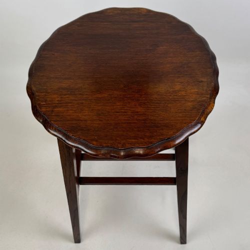 fig 6. A tall, dark oak Edwardian side table featuring a scalloped piecrust rim top, four splayed square legs, and a lower slatted shelf.
