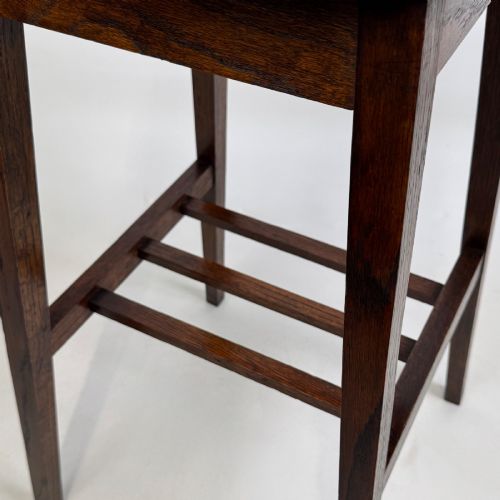 fig 7. A tall, dark oak Edwardian side table featuring a scalloped piecrust rim top, four splayed square legs, and a lower slatted shelf.