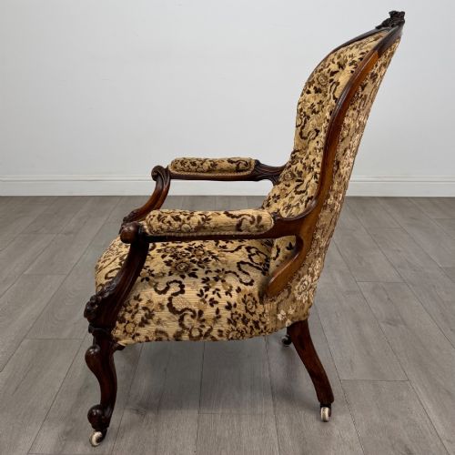 fig 1. A 19th-century Victorian open armchair constructed from carved walnut wood and upholstered in a patterned gold and brown velvet fabric.