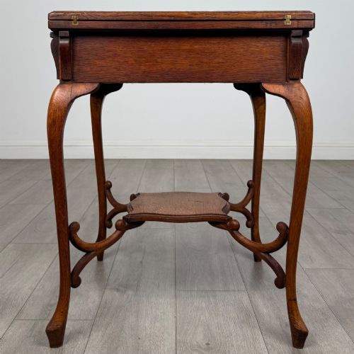 fig 2. An Edwardian oak envelope card table featuring cabriole legs, a decorative carved drawer front, and a shaped lower shelf.