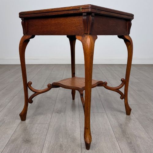 fig 3. An Edwardian oak envelope card table featuring cabriole legs, a decorative carved drawer front, and a shaped lower shelf.