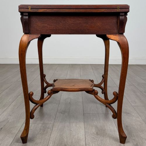 fig 4. An Edwardian oak envelope card table featuring cabriole legs, a decorative carved drawer front, and a shaped lower shelf.