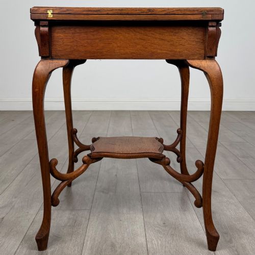 fig 6. An Edwardian oak envelope card table featuring cabriole legs, a decorative carved drawer front, and a shaped lower shelf.