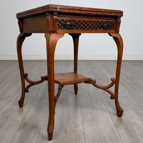 fig 7. An Edwardian oak envelope card table featuring cabriole legs, a decorative carved drawer front, and a shaped lower shelf.