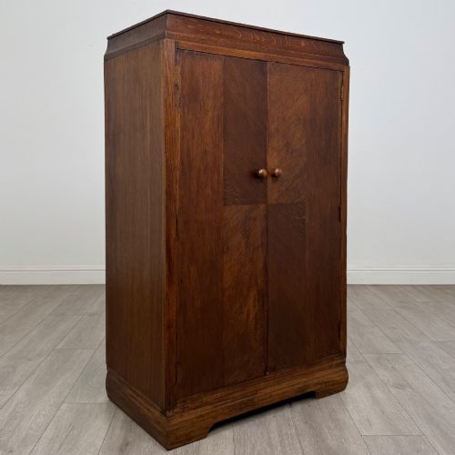 fig 8. A compact 20th-century oak fitted wardrobe with two doors featuring diagonal grain veneering, turned wooden knobs, and a stepped top profile.