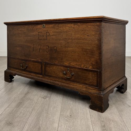 fig 1. An 18th-century Georgian golden oak mule chest featuring a hinged lid, two lower drawers with brass drop handles, shaped bracket feet, and the inscribed date 1789.