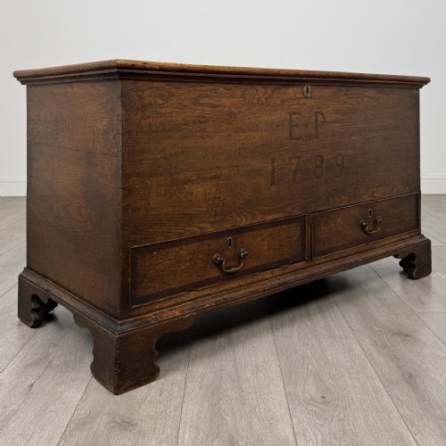 fig 7. An 18th-century Georgian golden oak mule chest featuring a hinged lid, two lower drawers with brass drop handles, shaped bracket feet, and the inscribed date 1789.