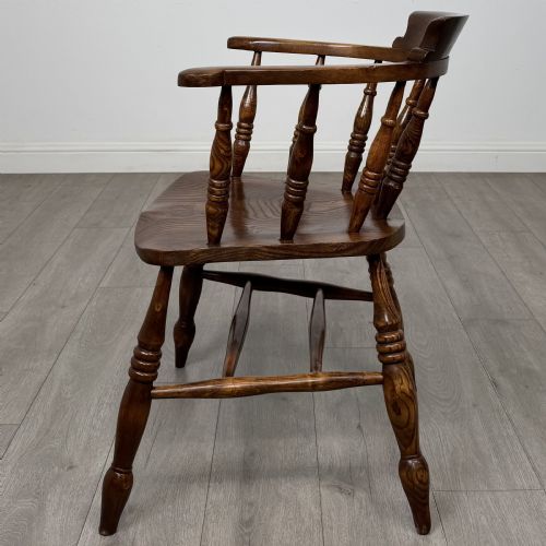 fig 1. A 20th-century antique elm smokers bow armchair featuring a horseshoe-shaped top rail, turned spindles, a shaped solid elm seat, and turned legs with H-stretchers.