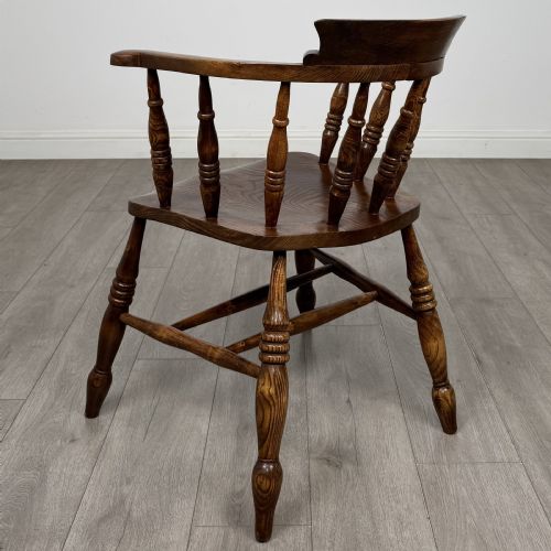 fig 2. A 20th-century antique elm smokers bow armchair featuring a horseshoe-shaped top rail, turned spindles, a shaped solid elm seat, and turned legs with H-stretchers.