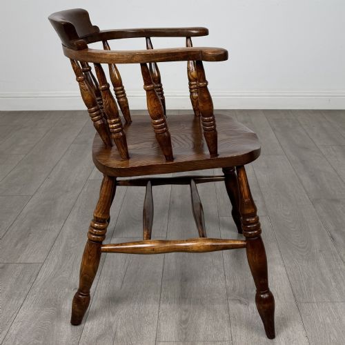fig 5. A 20th-century antique elm smokers bow armchair featuring a horseshoe-shaped top rail, turned spindles, a shaped solid elm seat, and turned legs with H-stretchers.