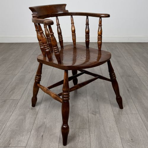 fig 6. A 20th-century antique elm smokers bow armchair featuring a horseshoe-shaped top rail, turned spindles, a shaped solid elm seat, and turned legs with H-stretchers.