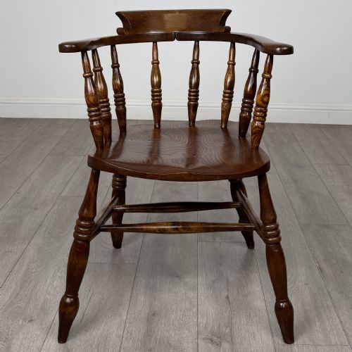 fig 7. A 20th-century antique elm smokers bow armchair featuring a horseshoe-shaped top rail, turned spindles, a shaped solid elm seat, and turned legs with H-stretchers.