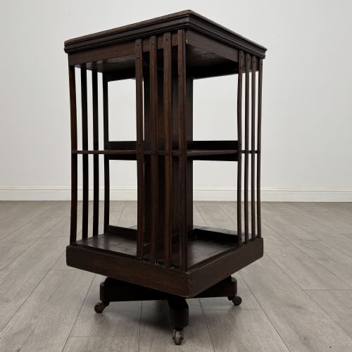 fig 1. A dark oak Edwardian revolving bookcase with vertical slatted sides, two shelf tiers, and a quadform base on castors.
