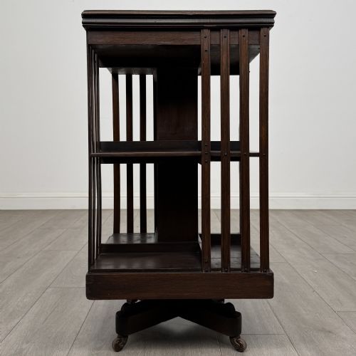 fig 2. A dark oak Edwardian revolving bookcase with vertical slatted sides, two shelf tiers, and a quadform base on castors.